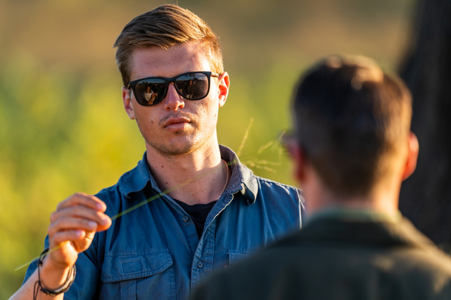 a-safari-guide-in-sunglasses-holds-a-blade-of-grass-while-speaking-to-a-guest.jpg