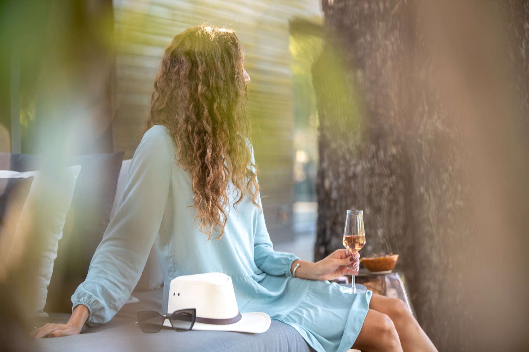 a-woman-in-a-blue-dress-sits-with-a-glass-of-wine-hat-and-sunglasses-beside-her.jpg